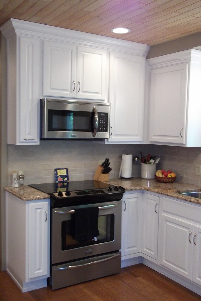 Example of a small classic l-shaped medium tone wood floor enclosed kitchen design in Other with an undermount sink, raised-panel cabinets, white cabinets, granite countertops, beige backsplash, ceramic backsplash, stainless steel appliances and no island