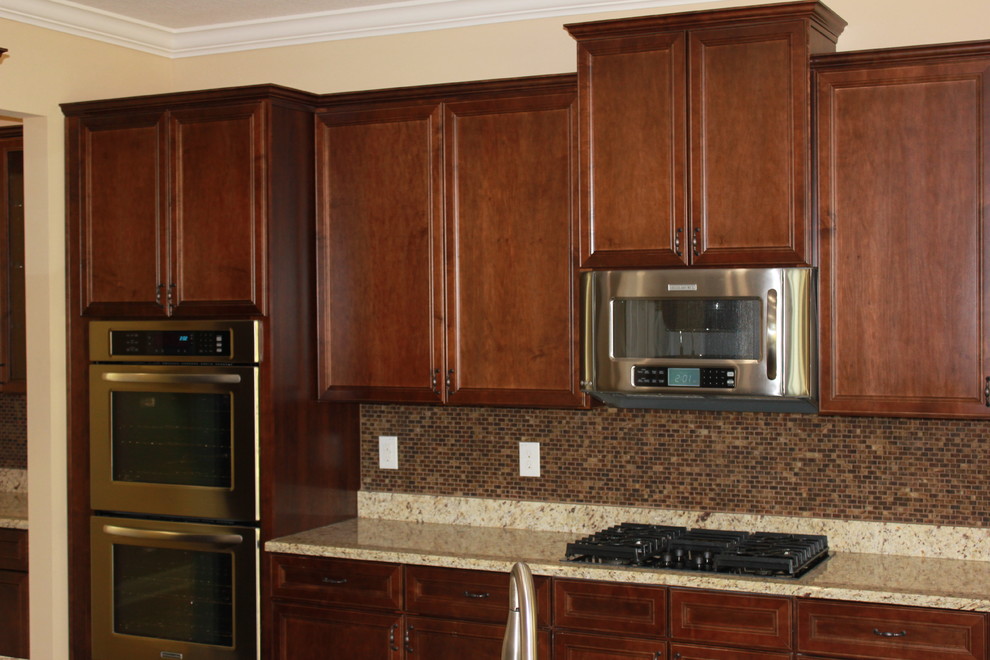Inredning av ett medelhavsstil kök, med en undermonterad diskho, luckor med upphöjd panel, skåp i mörkt trä, granitbänkskiva, brunt stänkskydd, stänkskydd i mosaik och rostfria vitvaror