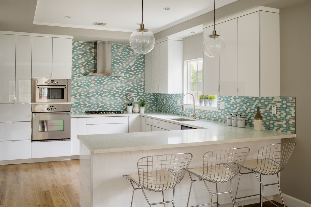 Mid-sized trendy u-shaped light wood floor eat-in kitchen photo in Los Angeles with a drop-in sink, flat-panel cabinets, white cabinets, granite countertops, blue backsplash, mosaic tile backsplash, stainless steel appliances and no island