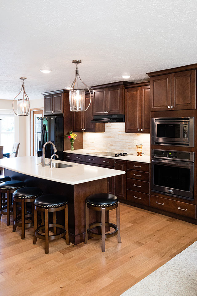 Foto på ett mellanstort vintage vit kök, med en undermonterad diskho, luckor med upphöjd panel, skåp i mörkt trä, bänkskiva i kvarts, beige stänkskydd, stänkskydd i porslinskakel, rostfria vitvaror, mellanmörkt trägolv, en köksö och brunt golv