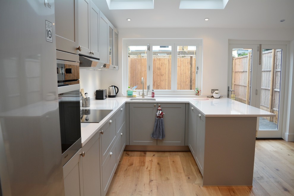 Inspiration for a mid-sized farmhouse u-shaped light wood floor open concept kitchen remodel in London with shaker cabinets, gray cabinets, solid surface countertops, stainless steel appliances, no island and a single-bowl sink