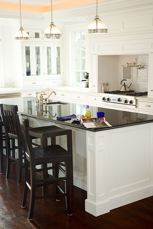 Klassisk inredning av ett stort kök, med en rustik diskho, vita skåp, vitt stänkskydd, rostfria vitvaror, mörkt trägolv och en köksö