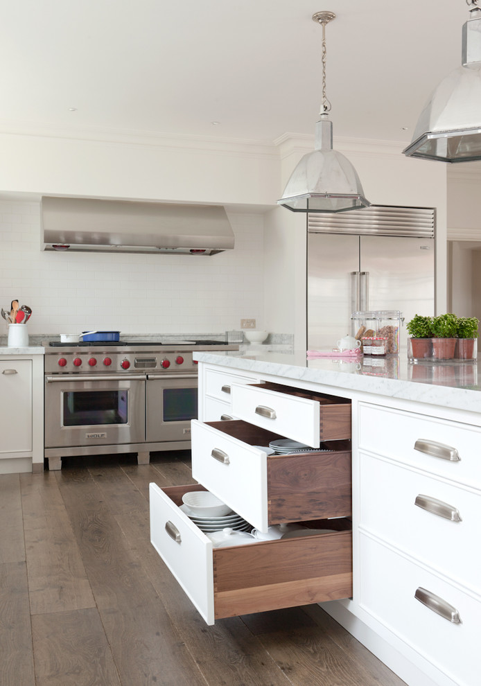 Klassische Wohnküche mit flächenbündigen Schrankfronten, weißen Schränken, Marmor-Arbeitsplatte, Küchenrückwand in Weiß, Rückwand aus Metrofliesen und Küchengeräten aus Edelstahl in Wiltshire
