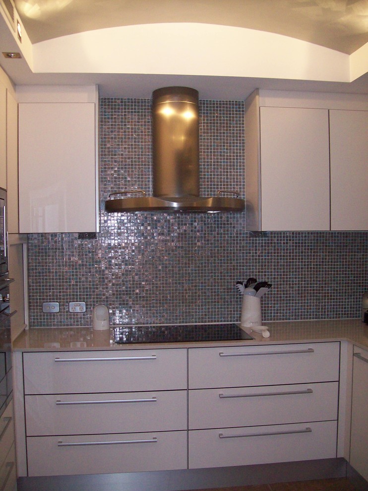 Bild på ett mellanstort funkis kök, med en nedsänkt diskho, vita skåp, bänkskiva i kvarts, stänkskydd med metallisk yta, stänkskydd i mosaik, rostfria vitvaror, klinkergolv i terrakotta och en halv köksö