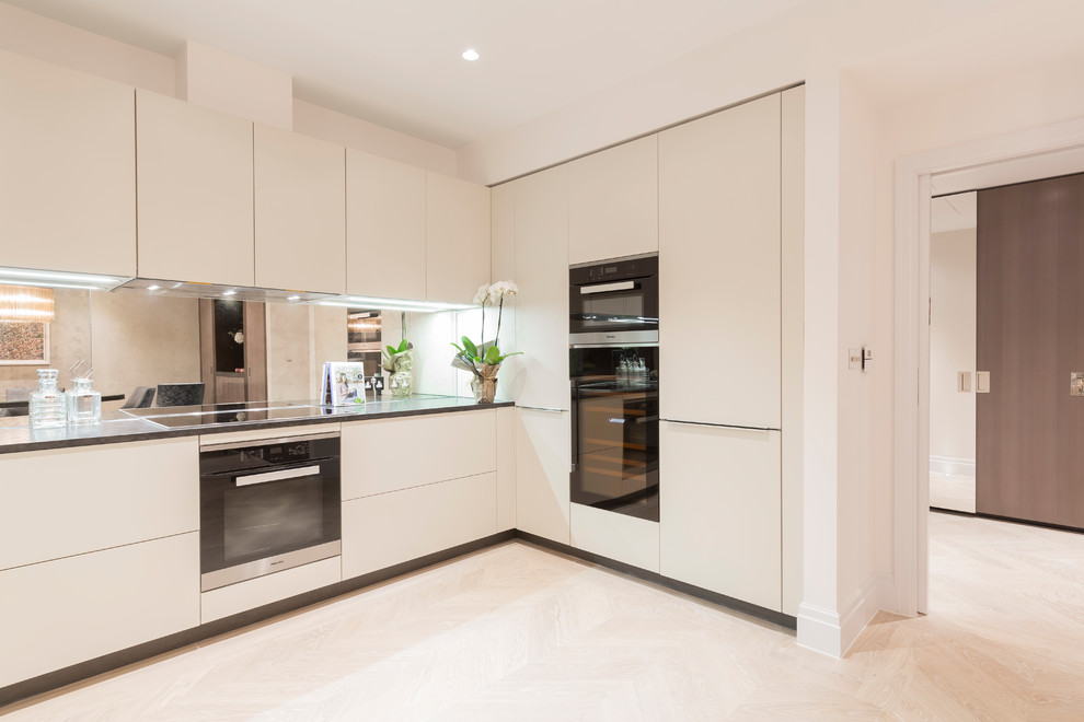 Foto di una grande cucina minimal con lavello integrato, ante lisce, ante beige, top in granito, paraspruzzi a specchio e elettrodomestici neri