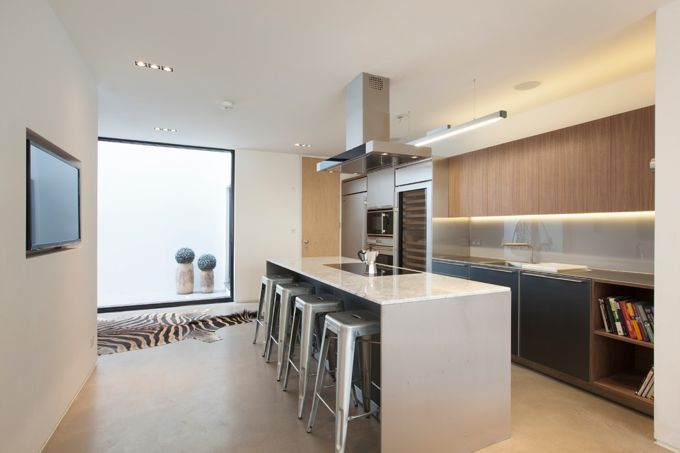Moderne Küche mit flächenbündigen Schrankfronten, hellbraunen Holzschränken, Küchenrückwand in Grau, Glasrückwand, Küchengeräten aus Edelstahl, Betonboden und Kücheninsel in London