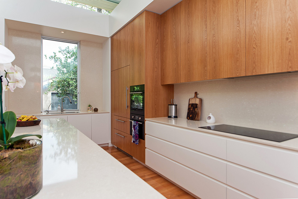 Mittelgroße Moderne Küche in U-Form mit Kücheninsel, hellbraunen Holzschränken, Granit-Arbeitsplatte, schwarzen Elektrogeräten, Unterbauwaschbecken und hellem Holzboden in Adelaide