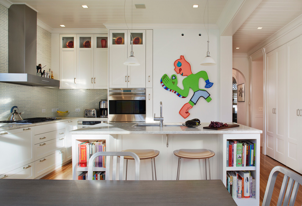 Cette photo montre une cuisine américaine chic en U avec un placard à porte shaker, des portes de placard blanches et une crédence grise.