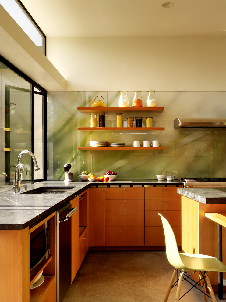 Exempel på ett modernt kök, med släta luckor, skåp i mellenmörkt trä, glaspanel som stänkskydd, en undermonterad diskho, grönt stänkskydd, rostfria vitvaror, betonggolv och en köksö