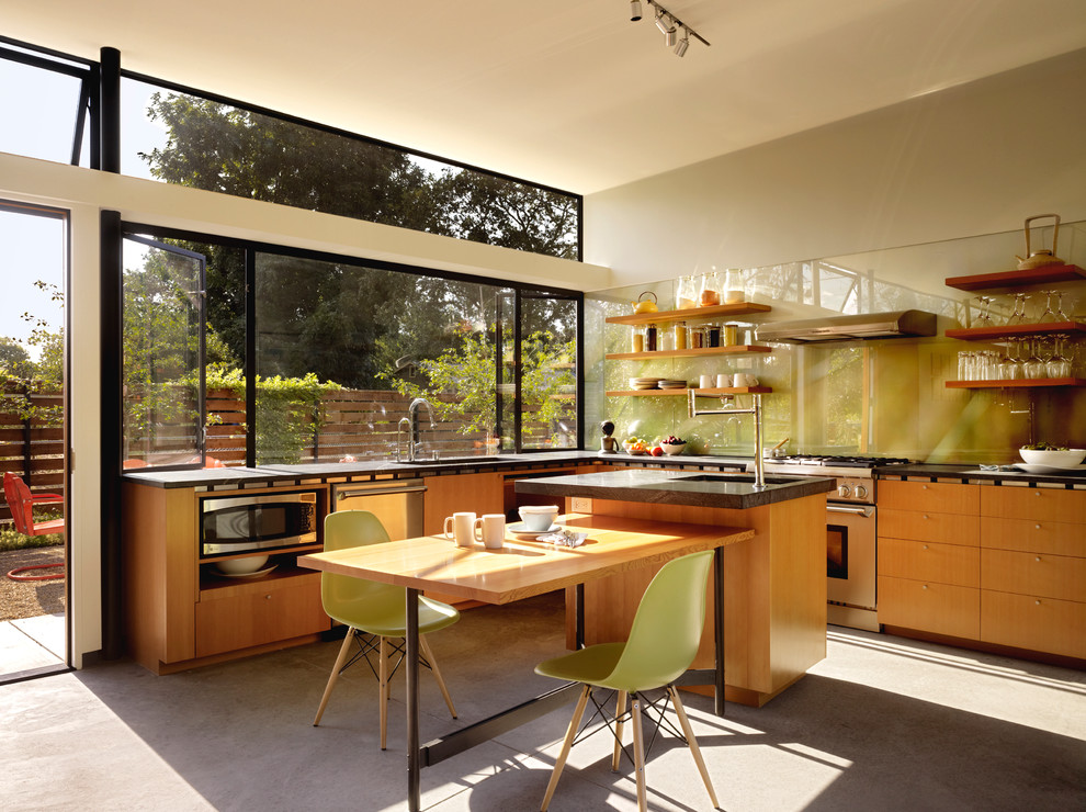 Idéer för ett modernt l-kök, med öppna hyllor, skåp i mellenmörkt trä, glaspanel som stänkskydd, rostfria vitvaror, en undermonterad diskho, grönt stänkskydd, betonggolv, en köksö och grått golv