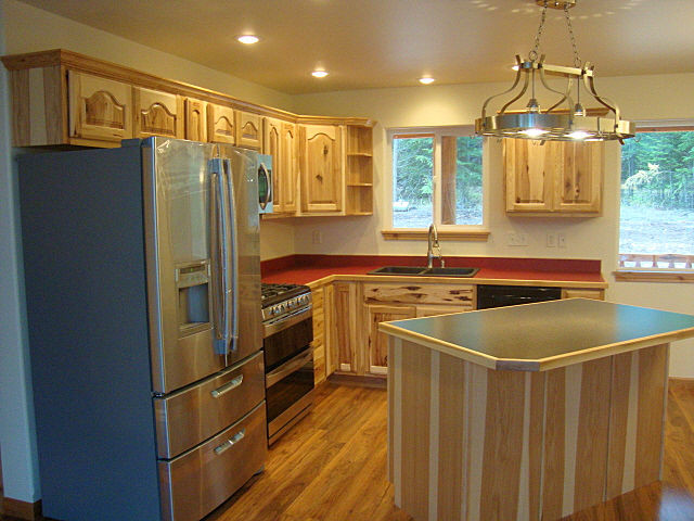 Example of a small mountain style l-shaped medium tone wood floor and brown floor eat-in kitchen design in Other with laminate countertops, red backsplash, an island, a double-bowl sink, raised-panel cabinets, light wood cabinets and stainless steel appliances