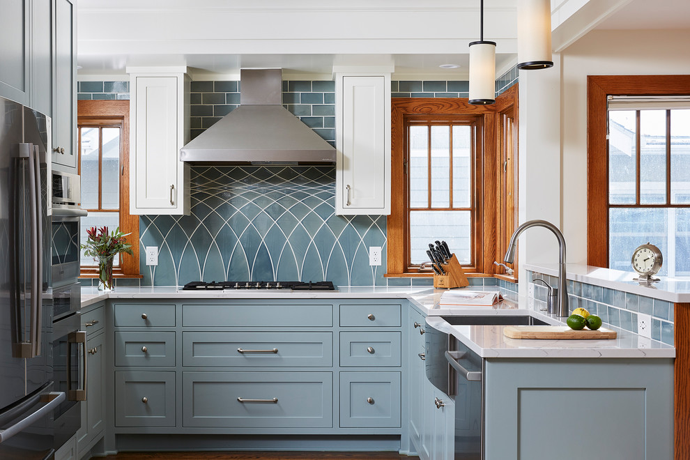 Inspiration pour une cuisine traditionnelle en U avec un évier de ferme, un placard à porte shaker, des portes de placard bleues, une crédence bleue, un électroménager en acier inoxydable et un plan de travail blanc.