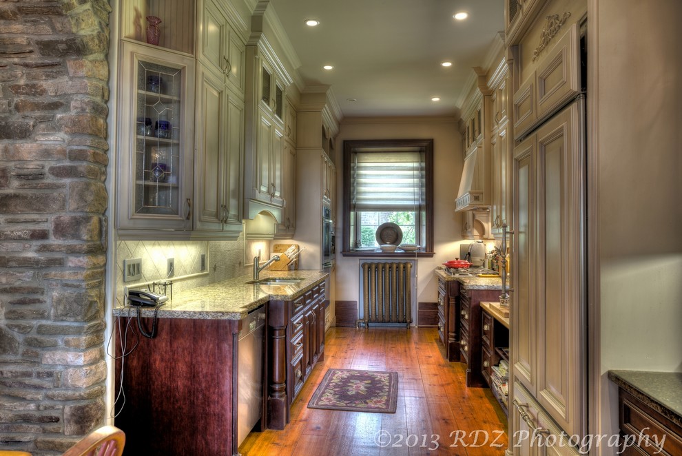 Klassisk inredning av ett kök, med en undermonterad diskho, skåp i ljust trä, granitbänkskiva, beige stänkskydd, stänkskydd i keramik och rostfria vitvaror
