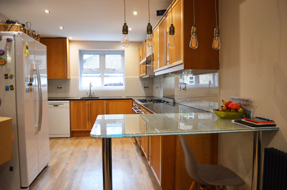 Bild på ett stort funkis kök och matrum, med släta luckor, bruna skåp, bänkskiva i glas, vitt stänkskydd, glaspanel som stänkskydd och en halv köksö