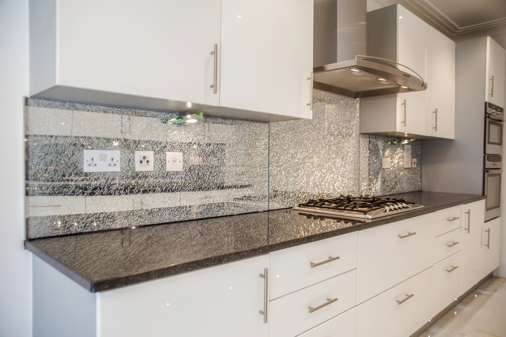 This is an example of a modern kitchen in Hertfordshire with glass sheet splashback.