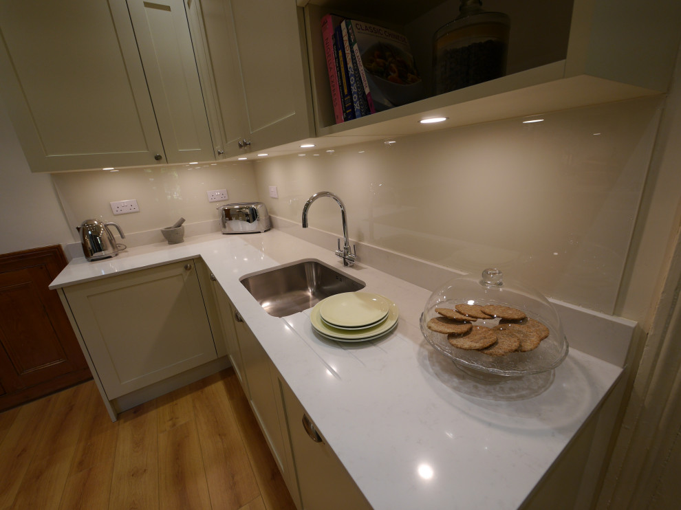 Medium sized contemporary galley kitchen in London with a submerged sink, shaker cabinets, green cabinets, quartz worktops, white splashback, glass sheet splashback, stainless steel appliances, laminate floors, no island, multi-coloured floors and white worktops.