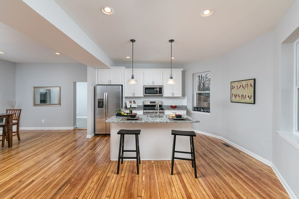 Example of a small classic single-wall medium tone wood floor and brown floor open concept kitchen design in Baltimore with an undermount sink, raised-panel cabinets, white cabinets, granite countertops, stainless steel appliances, an island and gray countertops