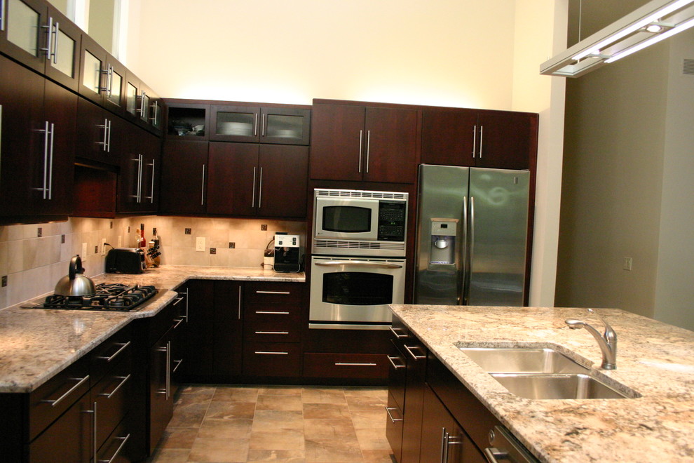 Modern inredning av ett l-kök, med en dubbel diskho, släta luckor, skåp i mörkt trä, granitbänkskiva, beige stänkskydd, rostfria vitvaror och en köksö