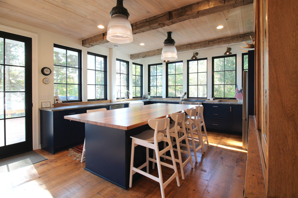 Foto på ett mellanstort maritimt brun kök, med en undermonterad diskho, skåp i shakerstil, blå skåp, träbänkskiva, brunt stänkskydd, fönster som stänkskydd, rostfria vitvaror, mellanmörkt trägolv, en köksö och brunt golv