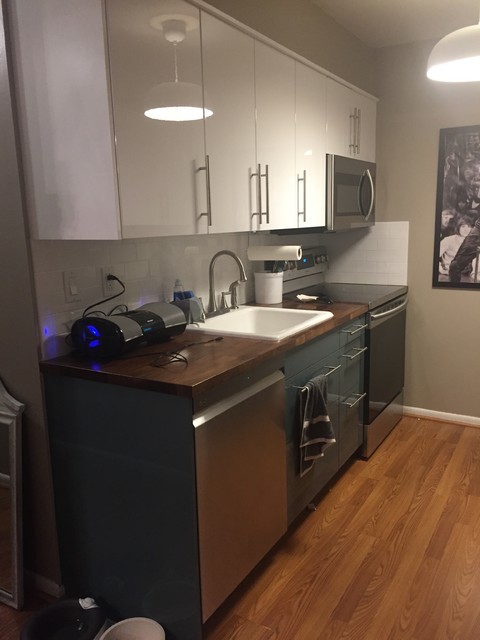 Photo of a small contemporary galley enclosed kitchen in New York with a built-in sink, flat-panel cabinets, turquoise cabinets, wood worktops, white splashback, ceramic splashback, stainless steel appliances, laminate floors, no island and brown floors.
