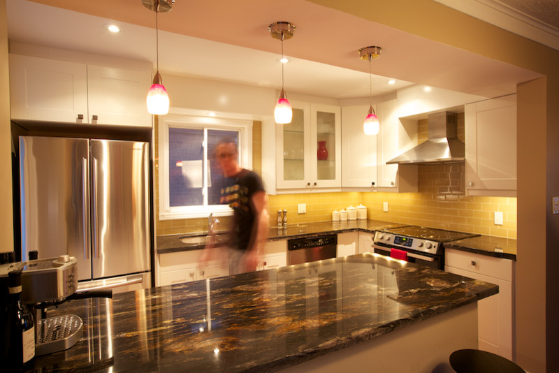 Cette image montre une cuisine américaine parallèle traditionnelle avec un évier 2 bacs, un placard à porte shaker, des portes de placard blanches, un plan de travail en granite, une crédence beige, un sol en bois brun et îlot.