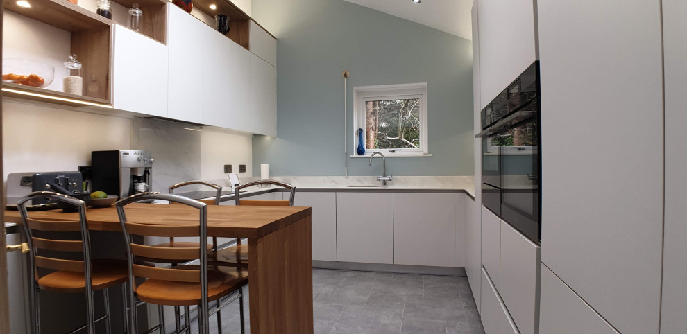 Foto di una grande cucina moderna con lavello sottopiano, ante lisce, ante bianche, top in onice, paraspruzzi bianco, elettrodomestici neri, pavimento in linoleum, pavimento grigio e top bianco