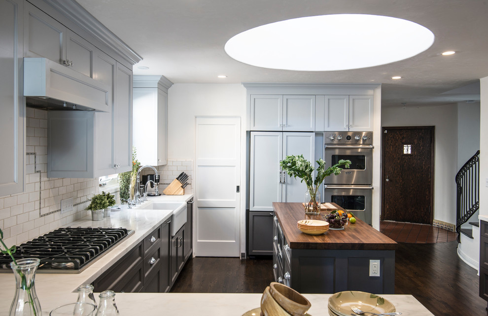 Inspiration for a traditional l-shaped kitchen in Los Angeles with a belfast sink, recessed-panel cabinets, blue cabinets, white splashback, metro tiled splashback, integrated appliances, dark hardwood flooring and an island.