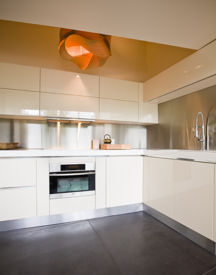 Idéer för att renovera ett mellanstort funkis kök, med en undermonterad diskho, släta luckor, vita skåp, stänkskydd med metallisk yta och rostfria vitvaror
