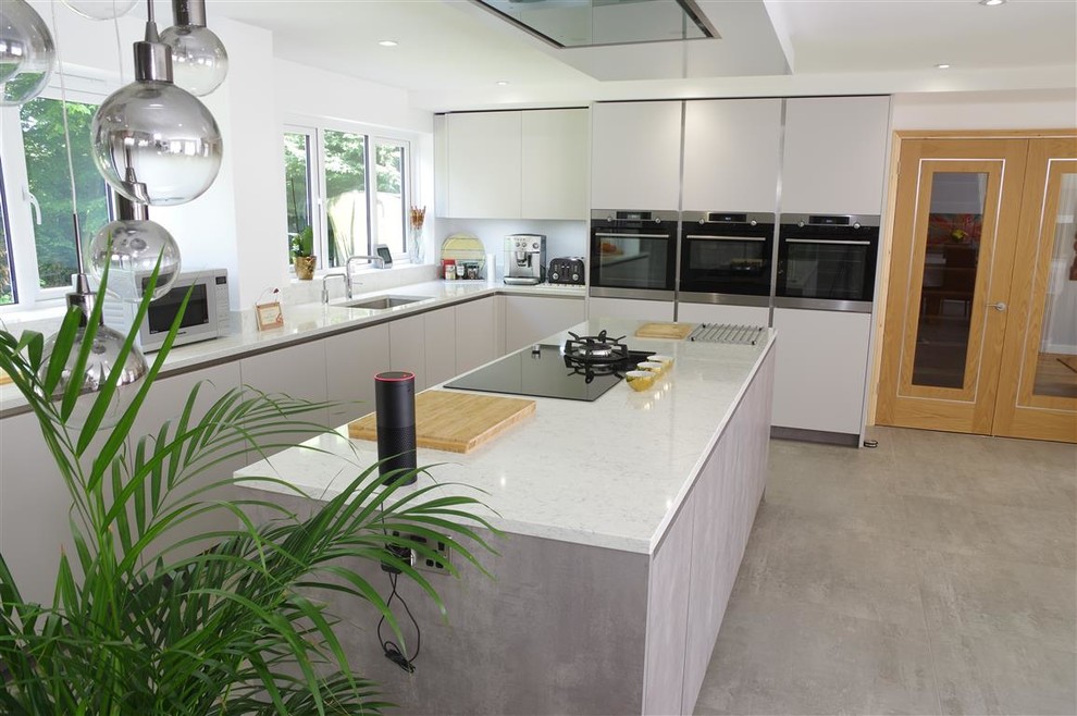 Inspiration for a modern kitchen in Kent with flat-panel cabinets, grey cabinets, black appliances, an island, grey floors and white worktops.