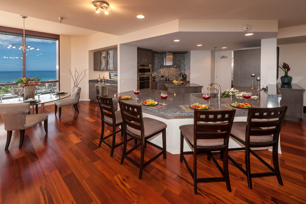 Example of a trendy kitchen design in Hawaii with a single-bowl sink, flat-panel cabinets, dark wood cabinets, solid surface countertops, multicolored backsplash, glass sheet backsplash, stainless steel appliances and an island
