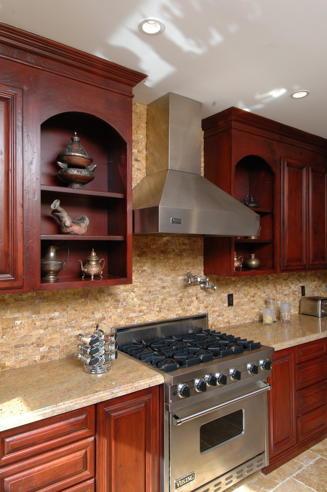 Klassisk inredning av ett stort kök, med luckor med upphöjd panel, skåp i mellenmörkt trä, granitbänkskiva, beige stänkskydd, stänkskydd i stenkakel, rostfria vitvaror och travertin golv