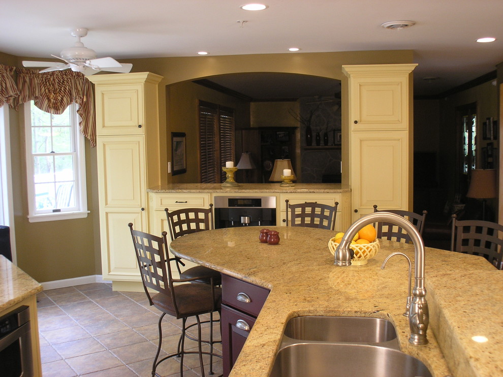 Exempel på ett stort klassiskt kök, med en dubbel diskho, luckor med upphöjd panel, gula skåp, granitbänkskiva, beige stänkskydd, stänkskydd i keramik, rostfria vitvaror, klinkergolv i keramik och en köksö