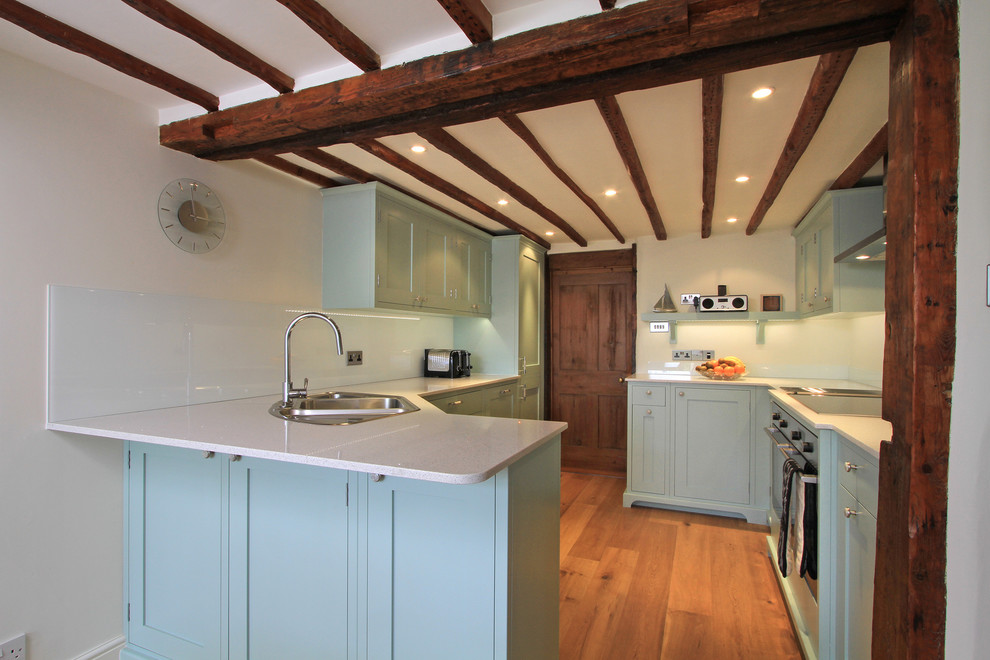 Classic kitchen in Hampshire with a built-in sink, blue cabinets, glass sheet splashback and engineered stone countertops.