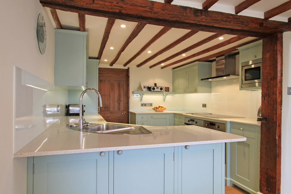 Пример оригинального дизайна: кухня в стиле неоклассика (современная классика) с накладной мойкой, синими фасадами, столешницей из кварцевого агломерата и фартуком из стекла