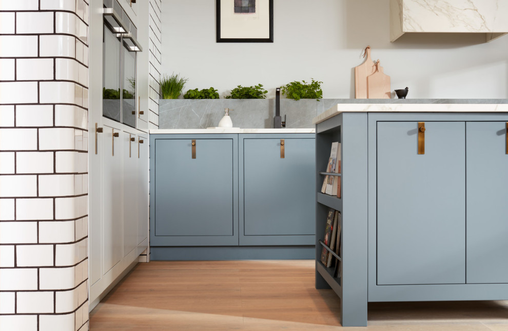 Inspiration for a medium sized contemporary l-shaped open plan kitchen in London with flat-panel cabinets, blue cabinets, marble worktops, grey splashback, stone slab splashback, light hardwood flooring, an island, brown floors and white worktops.