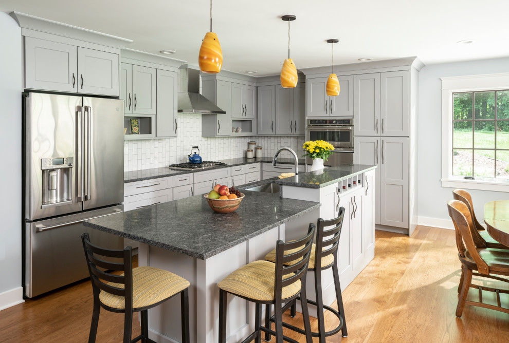Inredning av ett klassiskt stort grå grått kök, med en undermonterad diskho, skåp i shakerstil, grå skåp, bänkskiva i kvarts, vitt stänkskydd, stänkskydd i keramik, rostfria vitvaror, mellanmörkt trägolv, en köksö och brunt golv