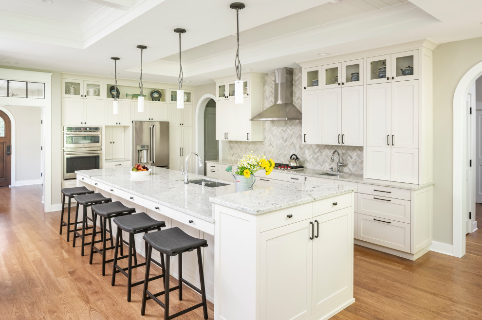 Photo of a large traditional l-shaped open plan kitchen in Detroit with a submerged sink, shaker cabinets, white cabinets, engineered stone countertops, grey splashback, stone tiled splashback, stainless steel appliances, medium hardwood flooring, an island, brown floors, grey worktops and a coffered ceiling.