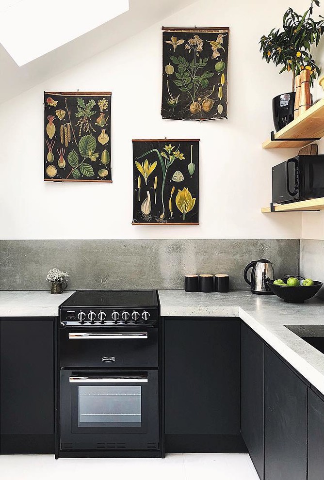 Modern inredning av ett litet grå grått kök, med en nedsänkt diskho, släta luckor, svarta skåp, bänkskiva i betong, grått stänkskydd, svarta vitvaror, målat trägolv och vitt golv