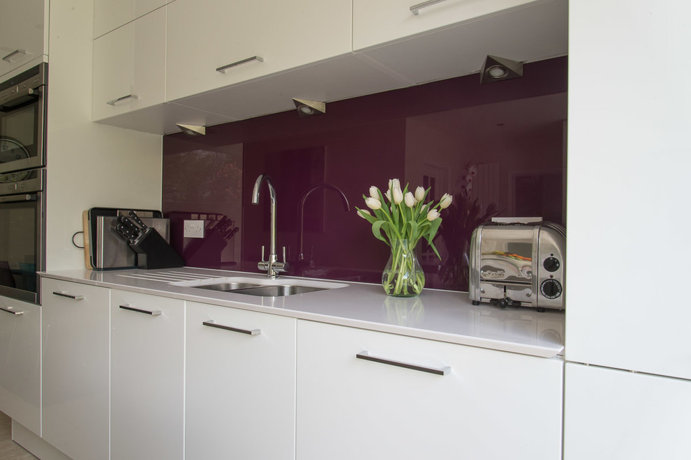 Foto di una cucina minimal di medie dimensioni con ante lisce, ante bianche, paraspruzzi con lastra di vetro e elettrodomestici in acciaio inossidabile