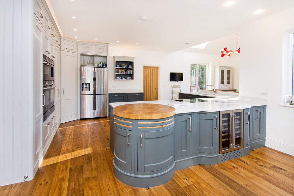 Klassisk inredning av ett stort vit vitt kök, med en enkel diskho, skåp i shakerstil, blå skåp, vitt stänkskydd, stänkskydd i sten, brunt golv, bänkskiva i kvartsit, svarta vitvaror, ljust trägolv och en köksö