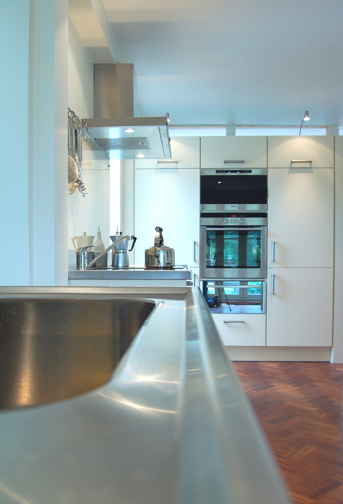 Aménagement d'une cuisine scandinave avec un évier intégré, un placard à porte plane, des portes de placard blanches, un plan de travail en inox, une crédence en feuille de verre, un électroménager en acier inoxydable et parquet foncé.
