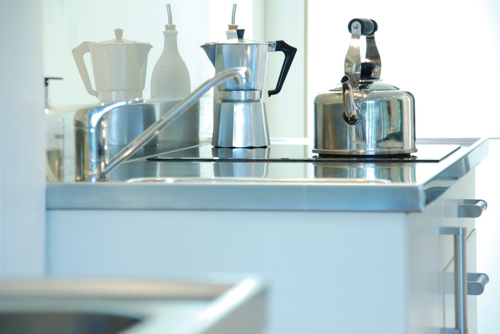 Nordische Küche mit integriertem Waschbecken, flächenbündigen Schrankfronten, weißen Schränken, Edelstahl-Arbeitsplatte, Glasrückwand, Küchengeräten aus Edelstahl und dunklem Holzboden in Surrey