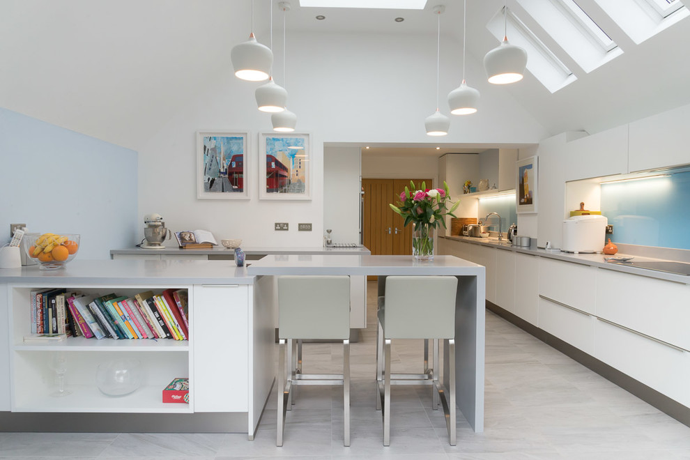 Photo of a large contemporary l-shaped kitchen/diner in Berkshire with flat-panel cabinets, white cabinets, composite countertops, blue splashback, glass sheet splashback, stainless steel appliances, porcelain flooring and a breakfast bar.