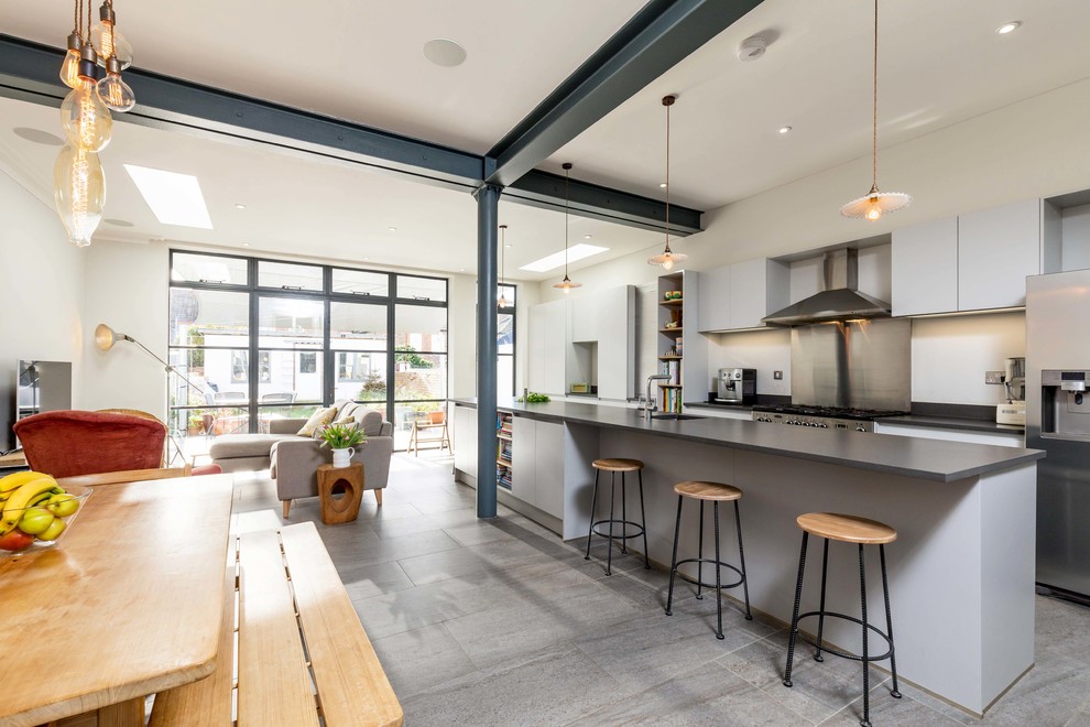 Foto på ett stort funkis svart linjärt kök med öppen planlösning, med släta luckor, grått stänkskydd, rostfria vitvaror, en köksö, grått golv, en undermonterad diskho, grå skåp och stänkskydd i metallkakel