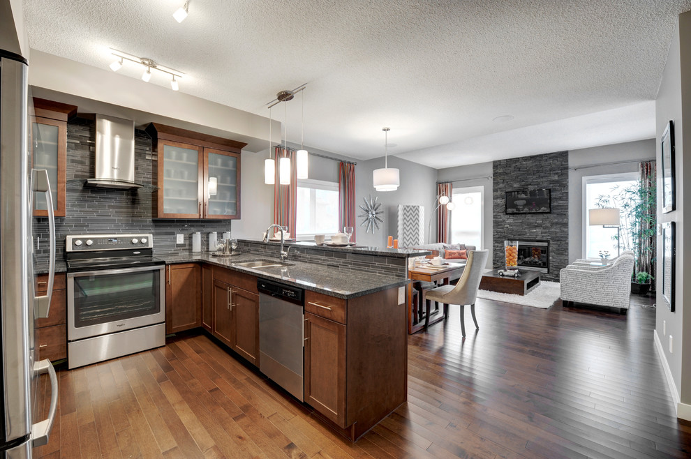 Inspiration for a mid-sized contemporary u-shaped medium tone wood floor eat-in kitchen remodel in Edmonton with an undermount sink, raised-panel cabinets, medium tone wood cabinets, granite countertops, black backsplash, stone tile backsplash, stainless steel appliances and a peninsula