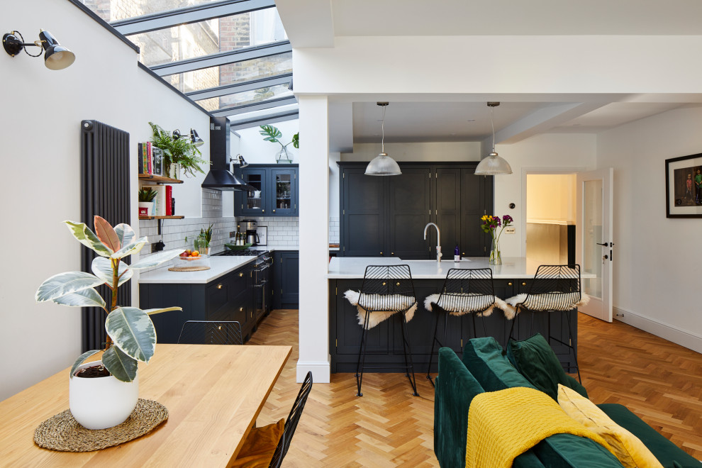 This is an example of a large contemporary l-shaped open plan kitchen in London with a double-bowl sink, blue cabinets, white splashback, stainless steel appliances, an island and white worktops.
