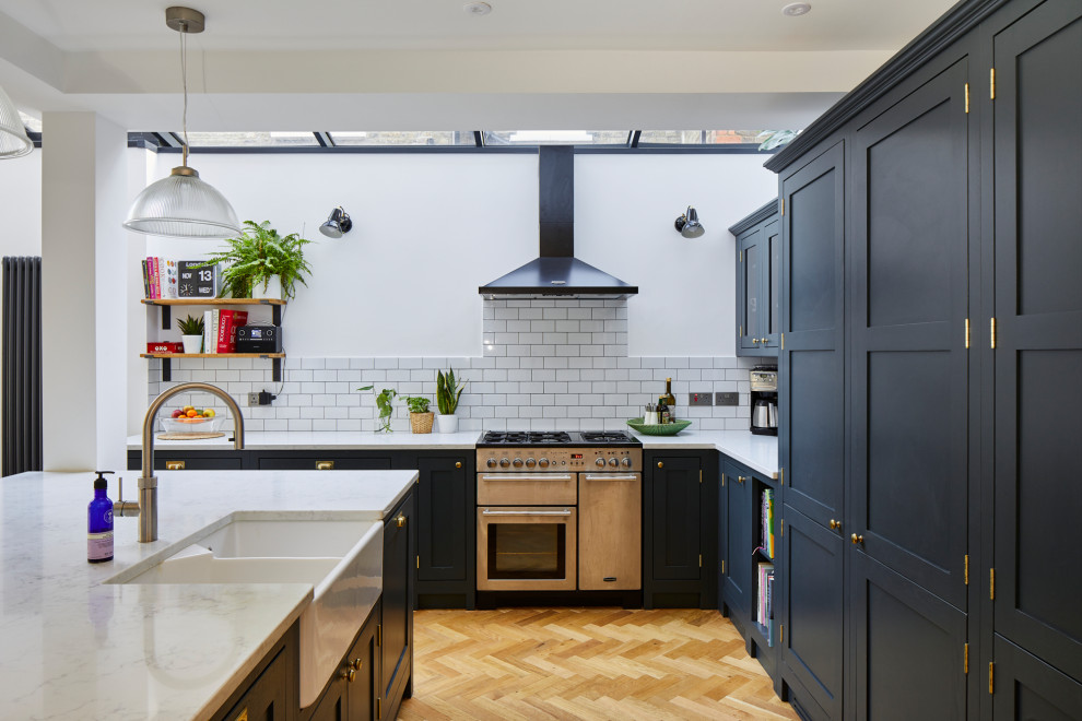 Offene, Große Moderne Küche in L-Form mit Doppelwaschbecken, blauen Schränken, Küchenrückwand in Weiß, Küchengeräten aus Edelstahl, Kücheninsel und weißer Arbeitsplatte in London