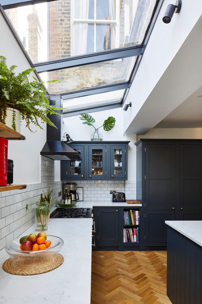 Photo of a large contemporary l-shaped open plan kitchen in London with a double-bowl sink, blue cabinets, white splashback, stainless steel appliances, an island and white worktops.