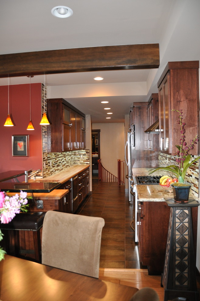 Example of a mid-sized transitional galley ceramic tile and brown floor eat-in kitchen design in Other with a double-bowl sink, shaker cabinets, dark wood cabinets, wood countertops, multicolored backsplash, matchstick tile backsplash, stainless steel appliances and no island