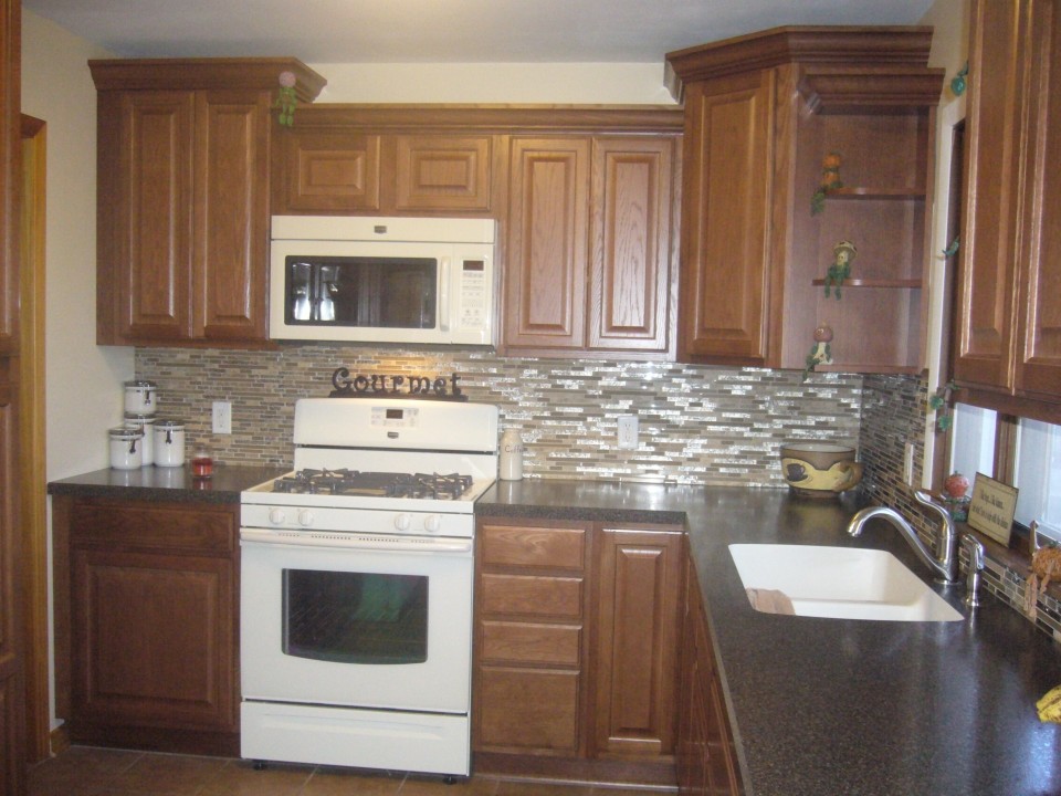 Bild på ett litet vintage kök, med en integrerad diskho, luckor med upphöjd panel, skåp i mellenmörkt trä, laminatbänkskiva, flerfärgad stänkskydd, stänkskydd i glaskakel, vita vitvaror och klinkergolv i keramik